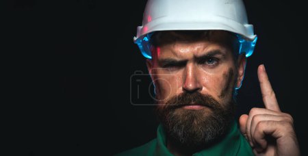 Closeup portrait of construction worker in hard hat pointing finger up. Bearded man protective helmet. Building solutions. Serious builder in hardhat having good idea. Copy space for advertising