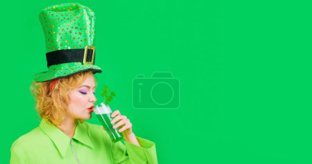 Sexy woman in leprechaun hat with glass of green beer. Beautiful girl in green jacket drinking beer at pub in Patricks day party. Traditional Irish festival. Copy space for Patricks day advertising