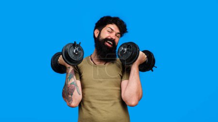Photo for Happy bearded man with dumbbells up in hands. Athletic muscular man lifting dumbbells in sport club. Strong sportsman doing workout in fitness gym. Weight training and bodybuilding. Sport equipment - Royalty Free Image