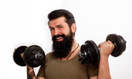 Photo for Smiling bearded man with dumbbells up in hands. Athletic muscular sportsman lifting dumbbells in sport club. Strong handsome bodybuilder doing workout in fitness gym. Weight training. Sport equipment - Royalty Free Image