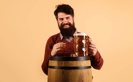 Beer time. Bearded man with mug of beer on wooden barrel. Smiling handsome male drinking beer. Germany traditions. Oktoberfest festival. Beer pub and bar. Holiday, drinks, alcohol and leisure concept