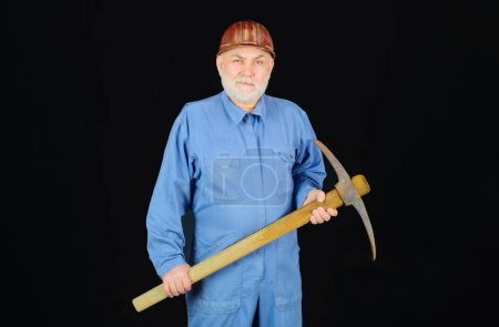 Photo for Construction and building works. Bearded man in coveralls and hard hat with pick-axe. Craftsman or contractor with pickaxe. Male builder in uniform and protective helmet with pick axe. Building tools - Royalty Free Image