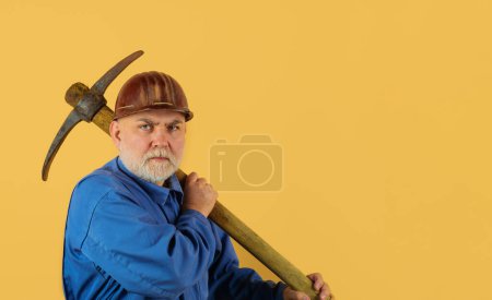 Photo for Serious bearded male builder in coveralls and hard hat with pick axe. Building tools. Craftsman, contractor or miner in uniform and protective helmet working with pick-axe. Copy space for advertising - Royalty Free Image