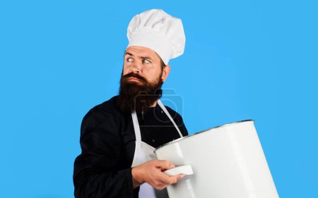 Photo for Cooking and culinary. Serious bearded man in chef hat and uniform with casserole or saucepan. Cookware, dinnerware, kitchenware and kitchen utensils concept. Male cook in apron with big pot or pan - Royalty Free Image