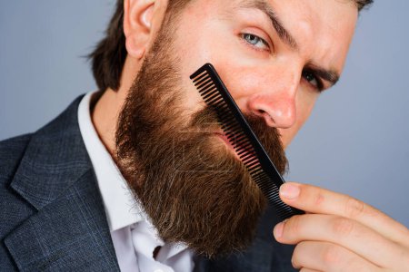 Barbershop. Stylish bearded man in suit combing beard with haircomb. Portrait of brutal man with beard and mustache with barber comb. Professional beard care. Barber shop advertising. Salon for men
