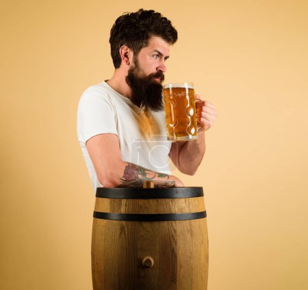 Beer time. Serious bearded man tasting draft beer. Pub or bar. Stylish handsome guy with mug of beer at restaurant. Alcohol drink. Oktoberfest festival. Wooden barrel with craft beer. Brewery concept