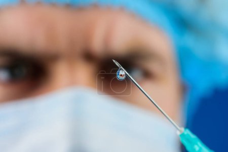 Vaccination. Doctor in medical mask with syringe preparing for injection. Needle closeup. Selective focus. Confident professional male physician hold syringe with dose of medicine working in hospital