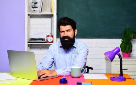 Photo for Male student studying online in university. Education and knowledge. Bearded teacher in classroom sitting at desk working on laptop computer. E-learning at college or high school. Online webinar - Royalty Free Image