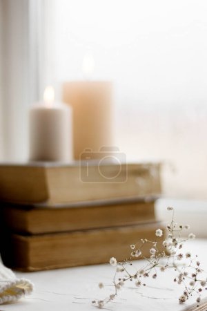 Téléchargez les photos : Livres anciens et bougies. Carte postale confortable. Fleurs blanches. Une photo romantique. Une décoration hivernale simple sur le rebord de la fenêtre. - en image libre de droit