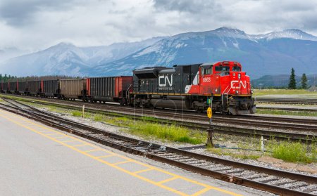 Photo for Jasper, Alberta, Canada - July 9, 2020: Canadian National CN Rail train engine pulling cargo through the town of Jasper in the Rocky Mountains. Canadian Rockies beautiful landscape - Royalty Free Image