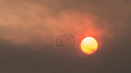Red sun hidden by smoke from wildfires. Thick smoky air pollution and climate change. Fiery sky environmental concerns from forest fires