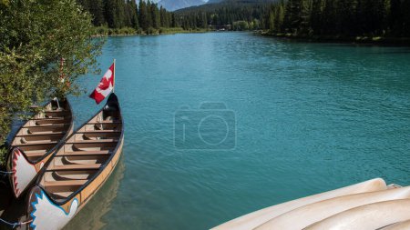 Foto de Bote en canoa atracado en la orilla. Agua turquesa del río Bow y fondo de la bandera de Canadá - Imagen libre de derechos