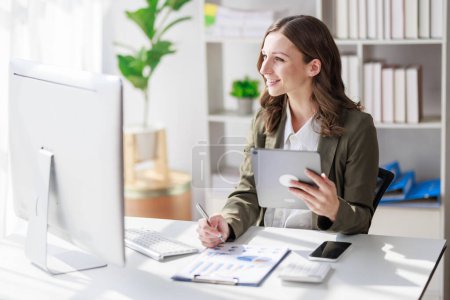 Photo for Concept of business office woman working,Businesswoman smile while working about her invesment plan with analyzing document and business investment graph data by using laptop on desk in workstation. - Royalty Free Image