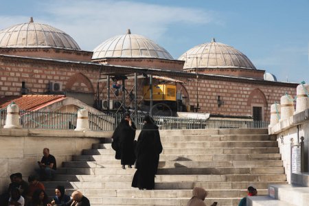 Téléchargez les photos : Istanbul, Turquie - 1er octobre 2022 : Des femmes musulmanes pieuses dans les burqas noires traditionnelles socialisent sur les marches devant une mosquée à Istanbul, en Turquie. - en image libre de droit