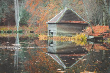 Photo for A colourful autuman woodland scene of an old abandoned boathouse over a calm still lake reflection on Loch Dunmore at Faskally Forest in Perth and Kinross, Scotland. - Royalty Free Image