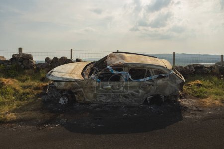 Foto de Escena de un accidente automovilístico con cinta policial en un accidente de coche quemado en una carretera rural en el Parque Regional Lomond Hills, Fife, Escocia, Reino Unido. - Imagen libre de derechos