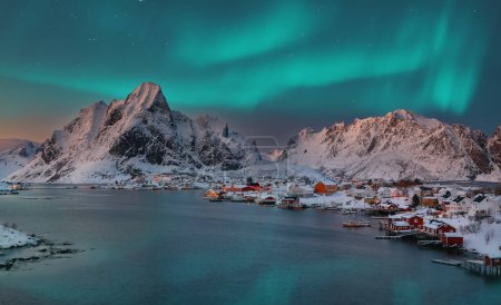 Dramatic evening cityscape of Reine town with Northern Lights. Red rorbuers on the shore of Reinefjorden. Popular travel destination on Lofotens. Location: Reine, Lofoten; Norway, Europe