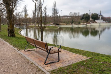 Photo for Wooden bench to sit and rest in a public park overlooking the crystal clear lake - Royalty Free Image