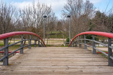 Téléchargez les photos : Large wooden bridge that crosses the lake of the public park where people walk quietly and play sports - en image libre de droit