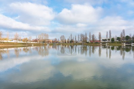 Téléchargez les photos : Panoramic view of a large lake in a public park where the cloudy sky and the trees of the shore are reflected, Tres Cantos, Madrid - en image libre de droit