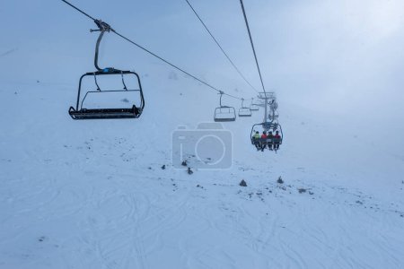 Foto de Chairlift that climbs the high mountain of the Pyrenees on a cloudy and snowy day with fog in Andorra, Grandvalira - Imagen libre de derechos