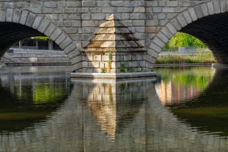 Stone arches of the old bridge reflected in the water of the Manzanares River, Madrid
