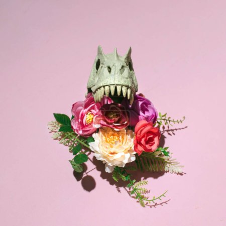 Dinosaur skull creatively decorated with colorful flowers, gothic inspired floral layout against pastel pink background.