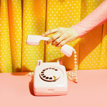 Old fashioned rotary dial telephone and female hand, creative nostalgic layout, retro aesthetic, pink and yellow background. 