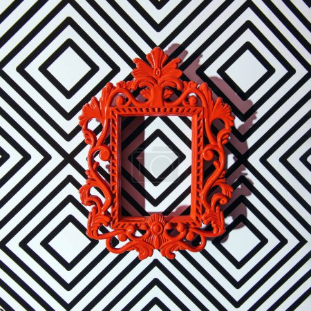 Antique style red frame against black and white geometric pattern wallpaper. Retro aesthetic, 1960s interior design idea.