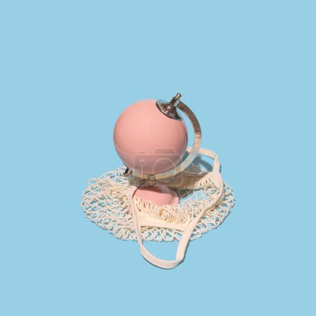 Photo for Pastel pink globe model in a retro style reusable shopping bag, creative aesthetic layout, pastel blue background. Summer holiday concept. - Royalty Free Image