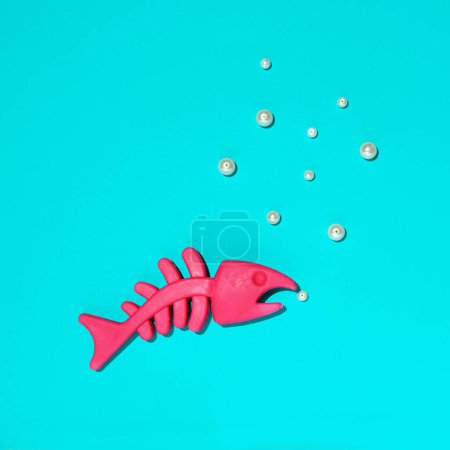 Tierspielzeug, rosafarbenes Fischskelett und Perlen, kreatives Unterwasserweltenkonzept. Leuchtend blauer Hintergrund.