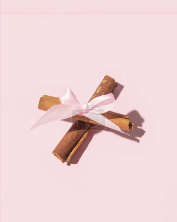 Photo for Two crossed cinnamon sticks decorated with a satin bow, Easter decoration on a pastel pink background. - Royalty Free Image