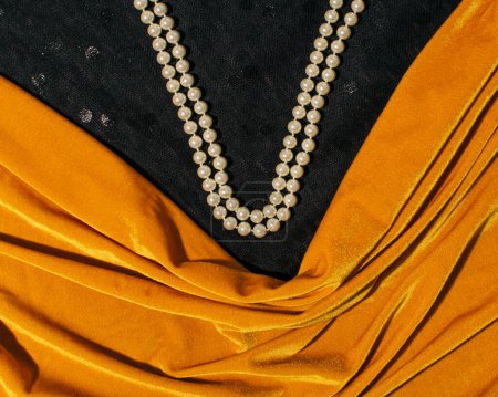 Bernsteingelber Samtstoff, drapiert, Perlenketten-Komposition auf schwarzem Hintergrund, femininer Ausschnitt, kreatives Konzept.