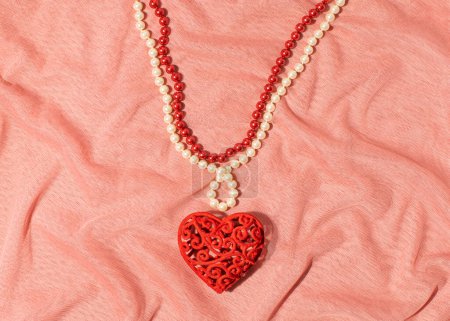 Necklace made of red and white strings of beads, big romantic heart as a pendant, creative aesthetic love and passion inspired layout, peach colored tulle background.