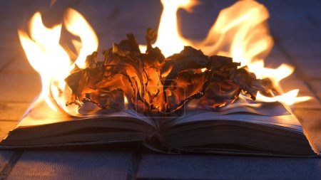 Ein offenes Buch steht in Flammen. Große helle Flamme, brennendes Papier auf alter Publikation im Dunkeln. Bücherverbrennung - Zensurkonzept