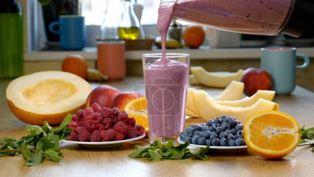 Himbeer-Blaubeer-Melonen-Smoothie wird in ein Glas auf dem Hintergrund frischer Früchte und Beeren gegossen. Der Fruchtcocktail ist fertig zum Essen. Gesundes und vegetarisches Ernährungskonzept