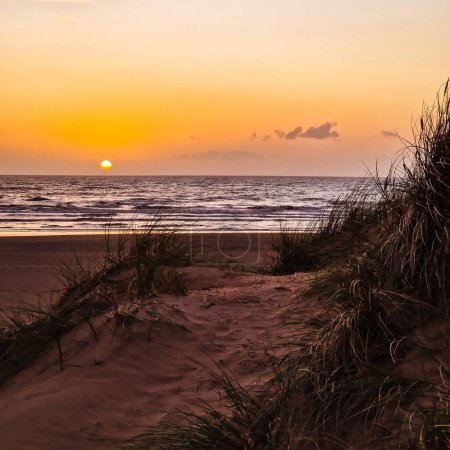 Téléchargez les photos : Le soleil plonge sous l'horizon, projetant une lueur dorée sur Formby Beach. - en image libre de droit
