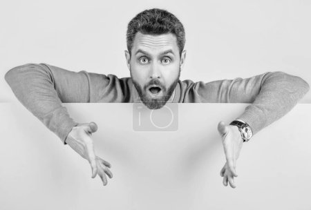 Photo for Surprised mature bearded man behind blank yellow paper banner with copy space for information gesturing, presenting product. - Royalty Free Image