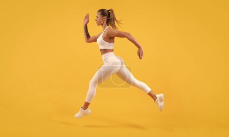 Foto de Energetic sport girl runner running on yellow background. - Imagen libre de derechos