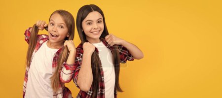 Happy children in casual checkered shirt hold long straight hair on yellow background, hair. Kid girl hair care, horizontal poster. Banner header with copy space