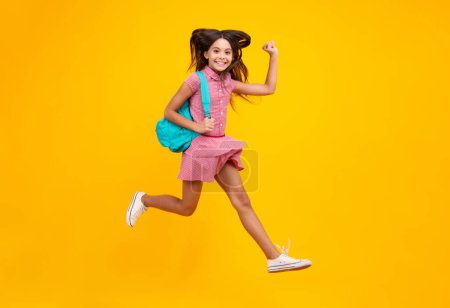 Téléchargez les photos : Schoolgirl in school uniform with backpack. Teenage girl student on yellow isolated background. Crazy run and jump. Learning and education children - en image libre de droit