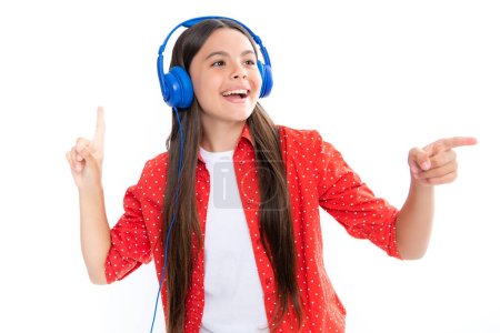 Foto de Teenager in modern wireless headphones enjoying song music in audio app, listening to her favorite music over white studio background. Happy teenager girl casual wear - Imagen libre de derechos