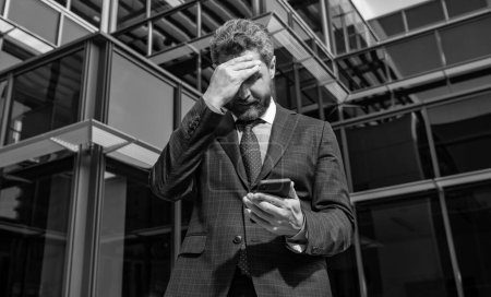 Foto de Nervous entrepreneur in businesslike suit looking at phone outside the office, anxiety. - Imagen libre de derechos