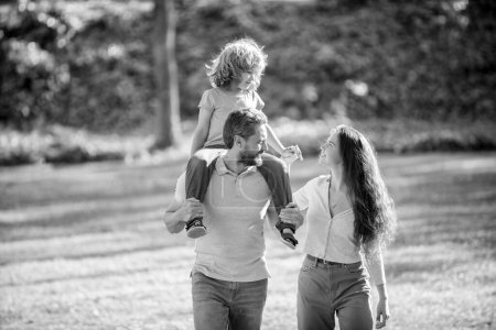Foto de Familia feliz de madre y padre llevando niño a hombros verano al aire libre, acogida. - Imagen libre de derechos