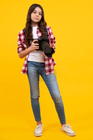 Teenager girl with dslr photo camera with zoom lens. Child photographer isoalted on yellow background. Photo school. Shooting with professional camera