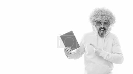 Photo for Crazy school teacher in funky orange wig and sunglasses point finger at blue book cover for copy space, schoolbook. - Royalty Free Image