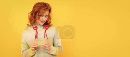 Téléchargez les photos : Woman isolated face portrait, banner with copy space. cheerful flirty redhead girl with red heart sticks on yellow background, love - en image libre de droit
