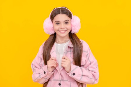 Téléchargez les photos : Mode adolescent fille sourire heureux en hiver chaud vêtements et cache-oreilles en fourrure fond jaune, à la mode. - en image libre de droit