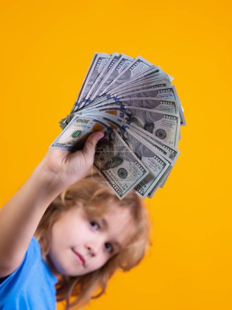 Téléchargez les photos : Enfant ayant beaucoup de cent dollars isolé sur fond jaune - en image libre de droit