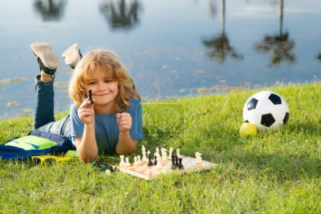 Foto de Niño concentrado desarrollando estrategia de ajedrez, jugando al juego de mesa en el patio trasero, tendido en la hierba - Imagen libre de derechos
